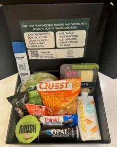 A black gift box filled with assorted healthy snacks, protein bars, chips, dried fruit, a beef stick, apple cinnamon mush, hydrating water, and info about workplace wellness services—perfect for Phoenix offices or self checkout kiosk setups.